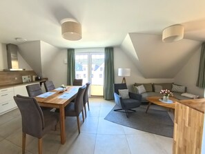 Un apartamento moderno con comedor, un conjunto de sofás, una mesa de centro y vistas a edificios a través de las ventanas.