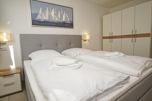 Une chambre d’hôtel comprenant un lit, une table de chevet, une lampe, une armoire et un tableau représentant des voiliers.