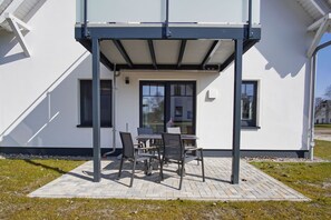 Ein modernes Haus mit überdachter Terrasse, einem Tisch und Stühlen sowie einem Fenster.