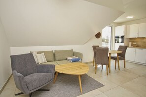A modern living room with a sofa, a coffee table, and a dining area with chairs. There is a kitchen visible through an open door. - Beachfront vacation rental with a balcony, pool access, and a sauna - Rex Rugia - Rex Rugia (Göhren)