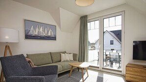 Ein modernes Wohnzimmer mit Sofa, Sessel, Couchtisch, Fernseher und einem Gemälde von Segelbooten.