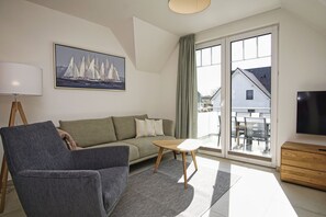 A modern living room with a sofa, a chair, a coffee table, a TV, and a painting of sailboats. - Beachfront vacation rental with a balcony, access to the pool and sauna - Rex Rugia H-1010 - (Göhren)