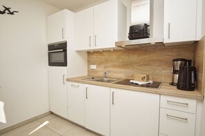 A modern kitchen with white cabinets, a built-in oven, a sink, and a coffee maker. - Beachfront vacation rental with a balcony, access to the pool and sauna - Rex Rugia - Rex Rugia (Göhren)