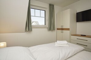 A bedroom with a bed, a window with curtains, a wardrobe, and a TV. - Beachfront vacation rental with a balcony, access to the pool and sauna - Rex Rugia - Rex Rugia (Göhren)