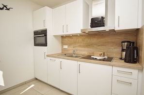 A modern kitchen with white cabinets, a built-in oven, a sink, and a coffee maker. - Beachfront vacation rental with a balcony, access to the pool and sauna - Rex Rugia H-1010 - (Göhren)