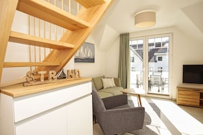 A modern living room with a wooden staircase, a sofa, a chair, and a TV.