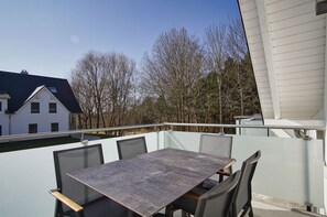 Ein Balkon mit Tisch und Stühlen, der auf einen Wohnbereich mit Bäumen und Häusern blickt.