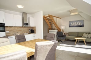 A modern kitchen with white cabinets, a wooden dining table, and a staircase leading to a loft area. - Beachfront vacation rental with a balcony, access to the pool and sauna - Rex Rugia H-1010 - (Göhren)