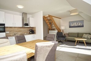 A modern kitchen with white cabinets, a wooden dining table, and a staircase leading to a loft area. - Beachfront vacation rental with a balcony, access to the pool and sauna - Rex Rugia - Rex Rugia (Göhren)
