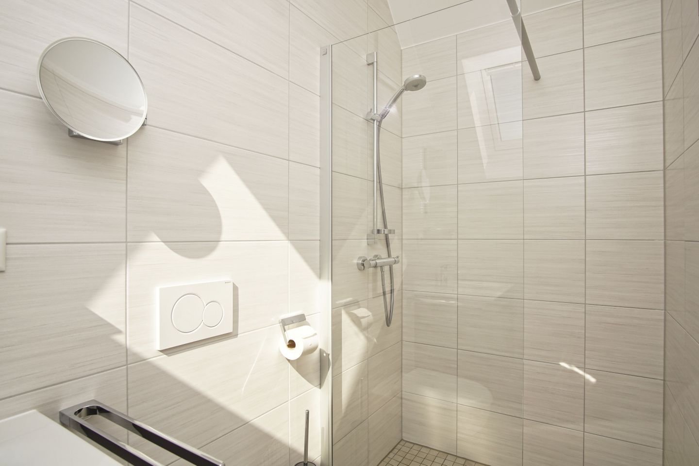 A modern bathroom with a glass shower enclosure, a wall-mounted mirror, and a towel rack.