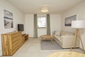 A modern living room with a wooden cabinet, a sofa, a coffee table, a lamp, and artwork on the walls. - Beachfront vacation rental with a terrace, pool access, and a sauna - Rex Rugia - Rex (Göhren)