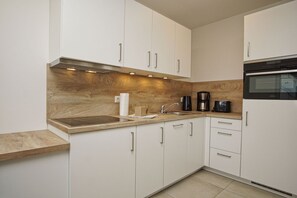 A modern kitchen with white cabinets, a wooden countertop, a built-in oven, and a coffee maker.