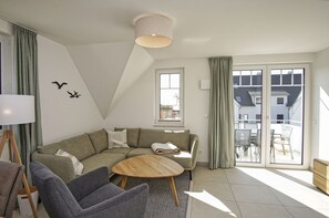A modern living room with a sectional sofa, a round coffee table, and a view of the outside balcony. - Beachfront vacation rental with a balcony, pool access, and a sauna - Rex Rugia - Rex Rugia (Göhren)