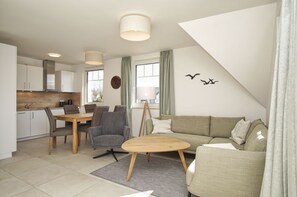 A modern living room with a sofa, a coffee table, and a dining area with chairs and a table. - Beachfront vacation rental with a balcony, pool access, and a sauna - Rex Rugia - Rex Rugia (Göhren)
