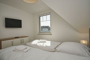 A bedroom with a bed, a TV mounted on the wall, a window with a view of houses, and a bedside lamp. - Beachfront vacation rental with a balcony, access to the pool and sauna - Rex Rugia - Rex Rugia (Göhren)