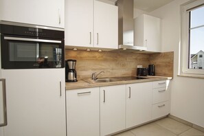 A modern kitchen with white cabinets, a stainless steel oven, a double sink, and a coffee maker.