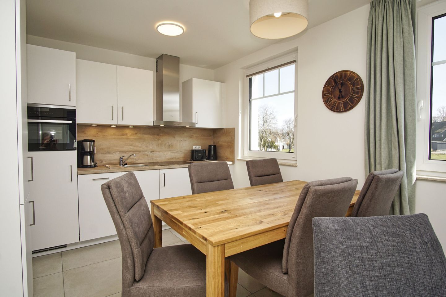 A modern kitchen with white cabinets, a wooden dining table, and grey upholstered chairs.