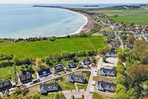 Vue aérienne d’une zone résidentielle côtière, avec des maisons, une plage et des champs verdoyants.