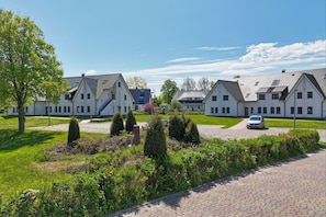 A row of modern, white houses with sloped roofs and multiple windows, surrounded by well-maintained lawns and a paved driveway.