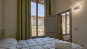 A bedroom with a large bed, a door leading to a balcony, and a window with curtains.