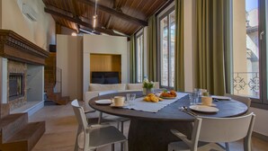 Un comedor con una mesa redonda, sillas blancas, una chimenea y vistas amplias por las ventanas.