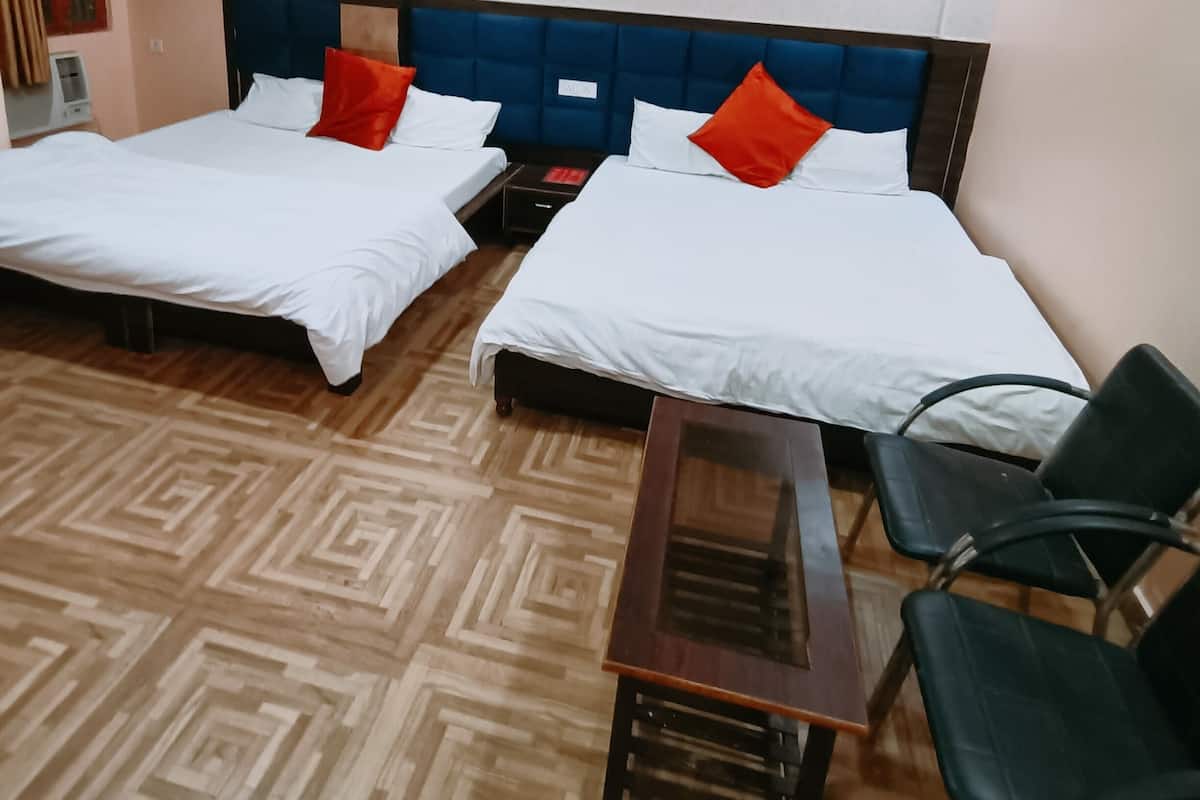 Habitació d'hotel amb dos llits, un terra de fusta, un ventilador de sostre i una taula petita amb cadires.