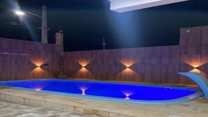 A swimming pool with a tiled deck, surrounded by a wooden wall with wall-mounted lights. - New House Tamandaré (Tamandaré)