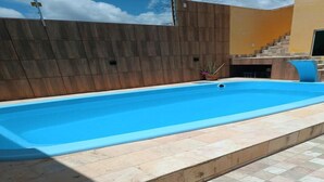 A rectangular swimming pool with a blue interior, surrounded by a tiled deck. - New House Tamandaré (Tamandaré)