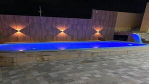A swimming pool with a tiled deck, surrounded by a wooden wall with built-in lighting. - New House Tamandaré (Tamandaré)