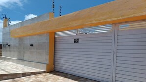 A modern building with a closed garage door, a concrete facade, and a tiled patio area. - New House Tamandaré (Tamandaré)
