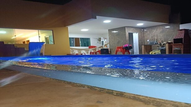 A swimming pool with a blue water feature, a modern building with a glass facade, and a brick fireplace. - New House Tamandaré (Tamandaré)