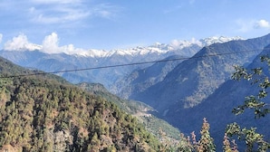 Paesaggio montuoso con cielo sereno, linee elettriche e una fitta foresta.