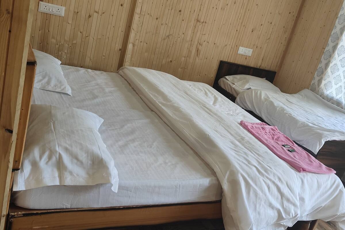 Zwei Einzelbetten mit Holz Kopfteilen in einem Zimmer mit Holzwänden und einem Fenster mit gemusterten Vorhängen.
