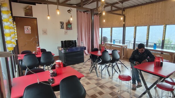 Un ristorante con tavoli rossi e sedie nere, interni in legno e una vista attraverso ampie finestre.
