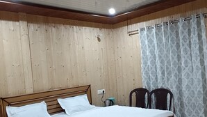 Una camera da letto con un letto in legno, una ventola a soffitto, una finestra con tende a motivi decorativi e un pavimento in legno.