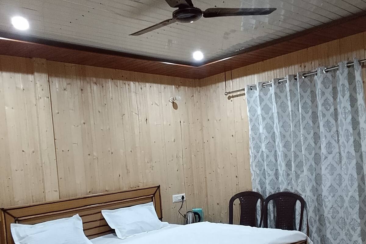 Ein Schlafzimmer mit einem Holzbett, einem Deckenventilator, einem Fenster mit gemusterten Vorhängen und einem Holzboden.