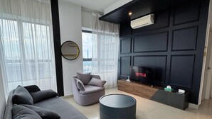 A modern living room with a grey sectional sofa, a round ottoman, a grey armchair, and a black entertainment unit with a TV displaying 'NETFLIX'. - Comfy Arte Plus Ampang City 7PAX-3BR-2CP (Kuala Lumpur)