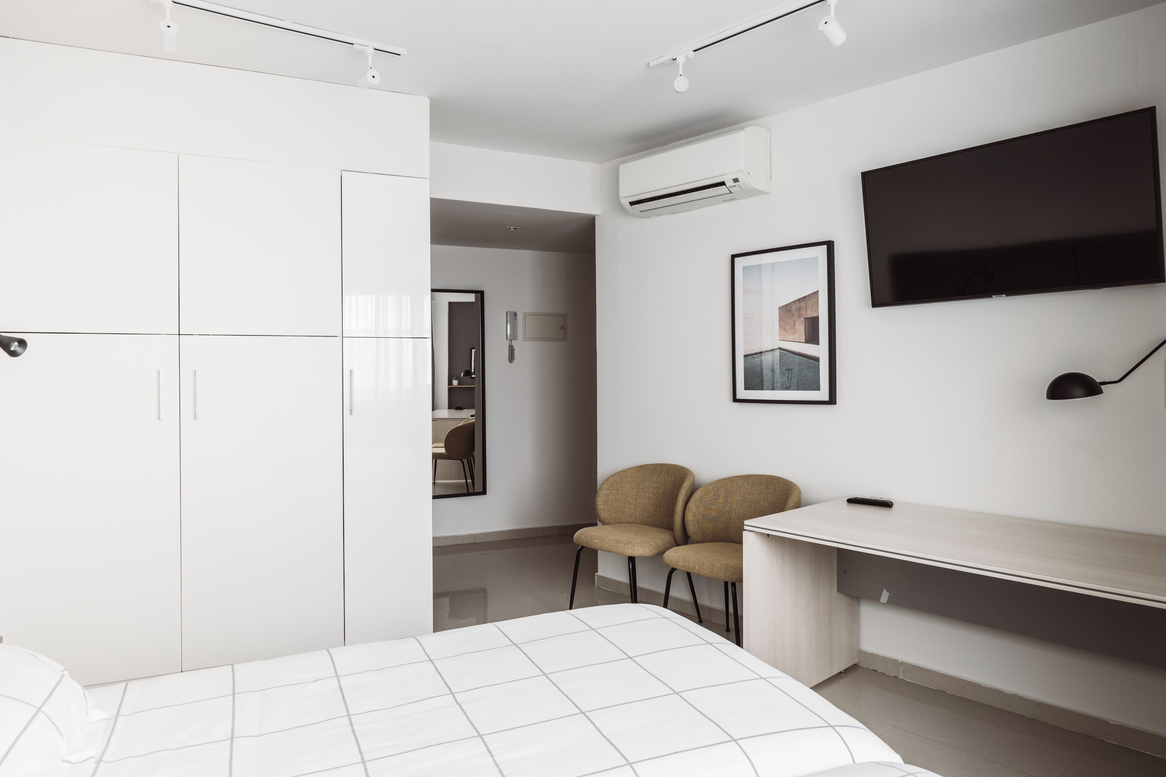 A modern bedroom with a bed, wardrobe, desk, chairs, and a TV.