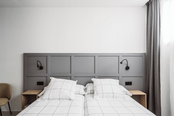 A modern bedroom with a grey headboard, two bedside tables, a chair, and a bed with white bedding.