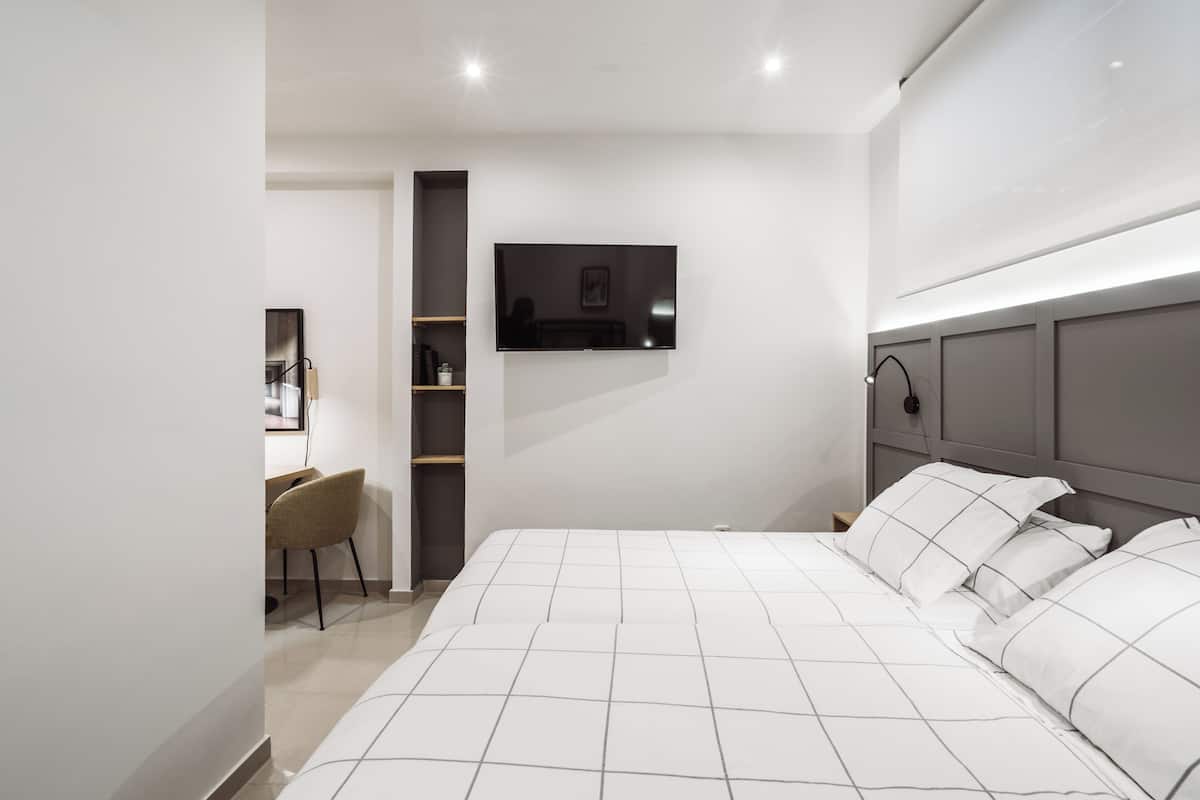 A modern bedroom with a large bed, a TV mounted on the wall, and a desk with a chair.