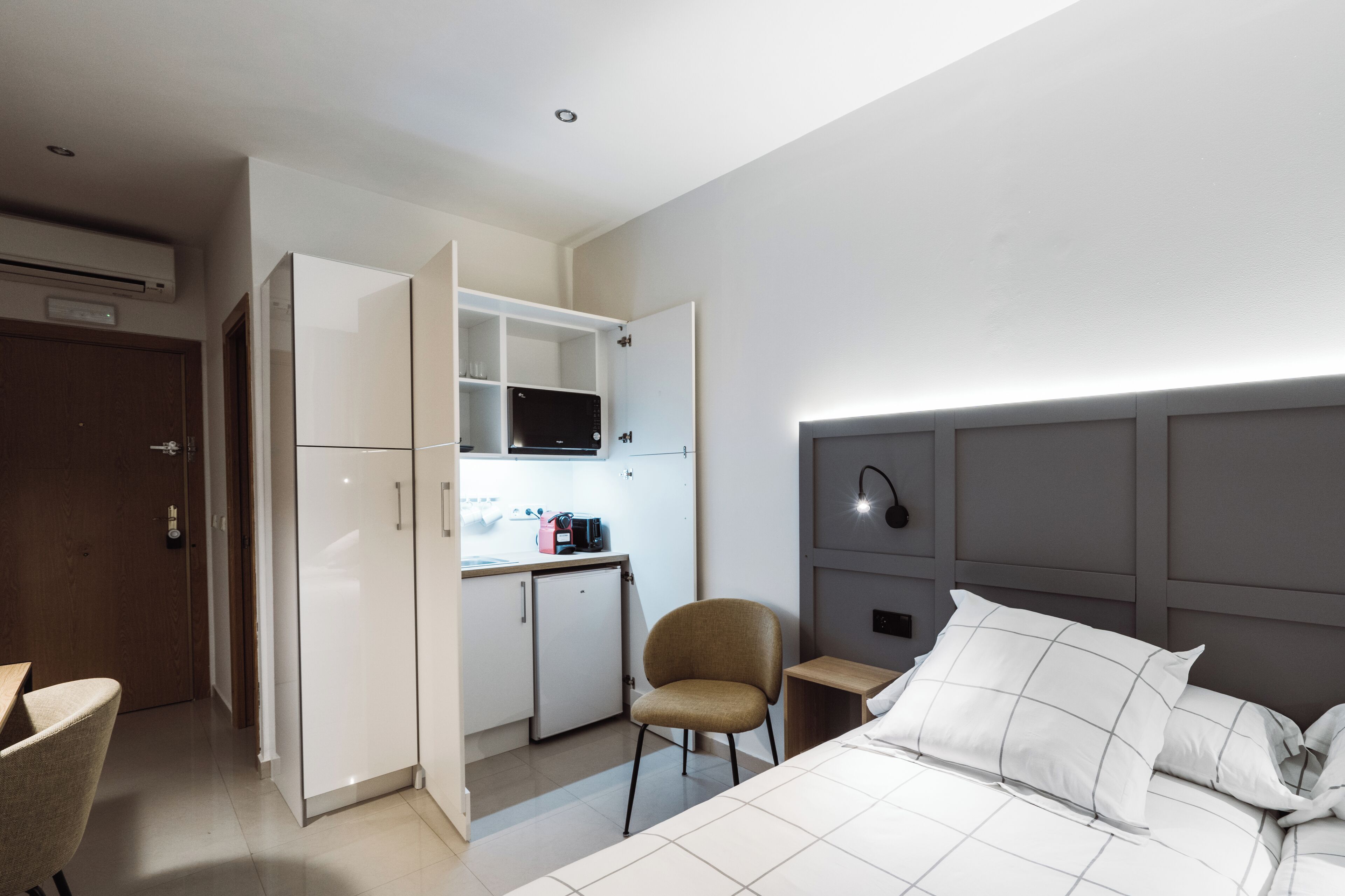 Et lille hotelværelse med seng, tekøkken, stol og skrivebord.