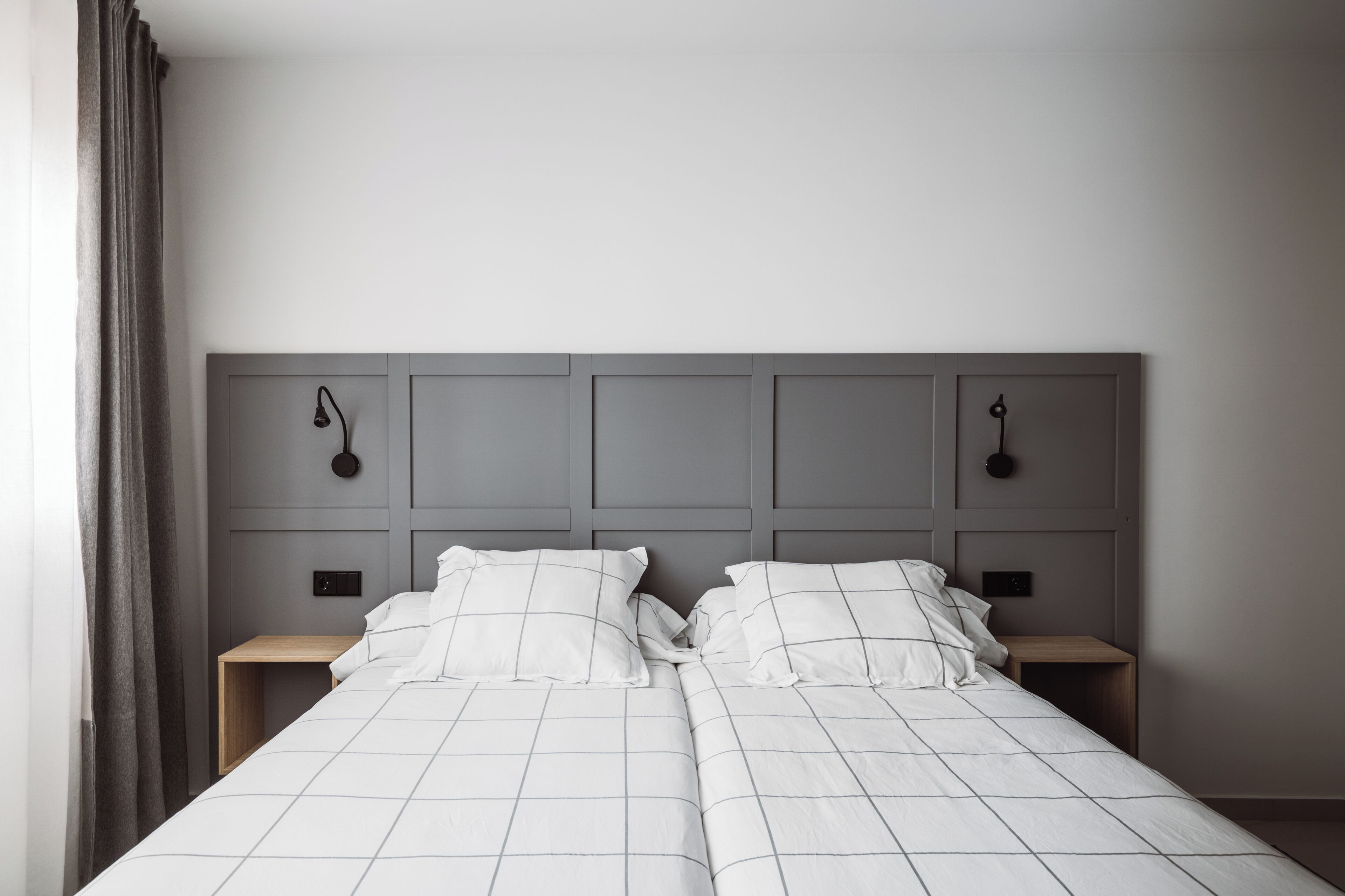 A double bed with a grey headboard, two bedside tables, and a grey curtain.