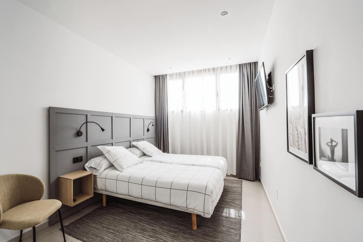 A modern hotel room with a bed, a chair, a TV, and framed pictures on the wall.