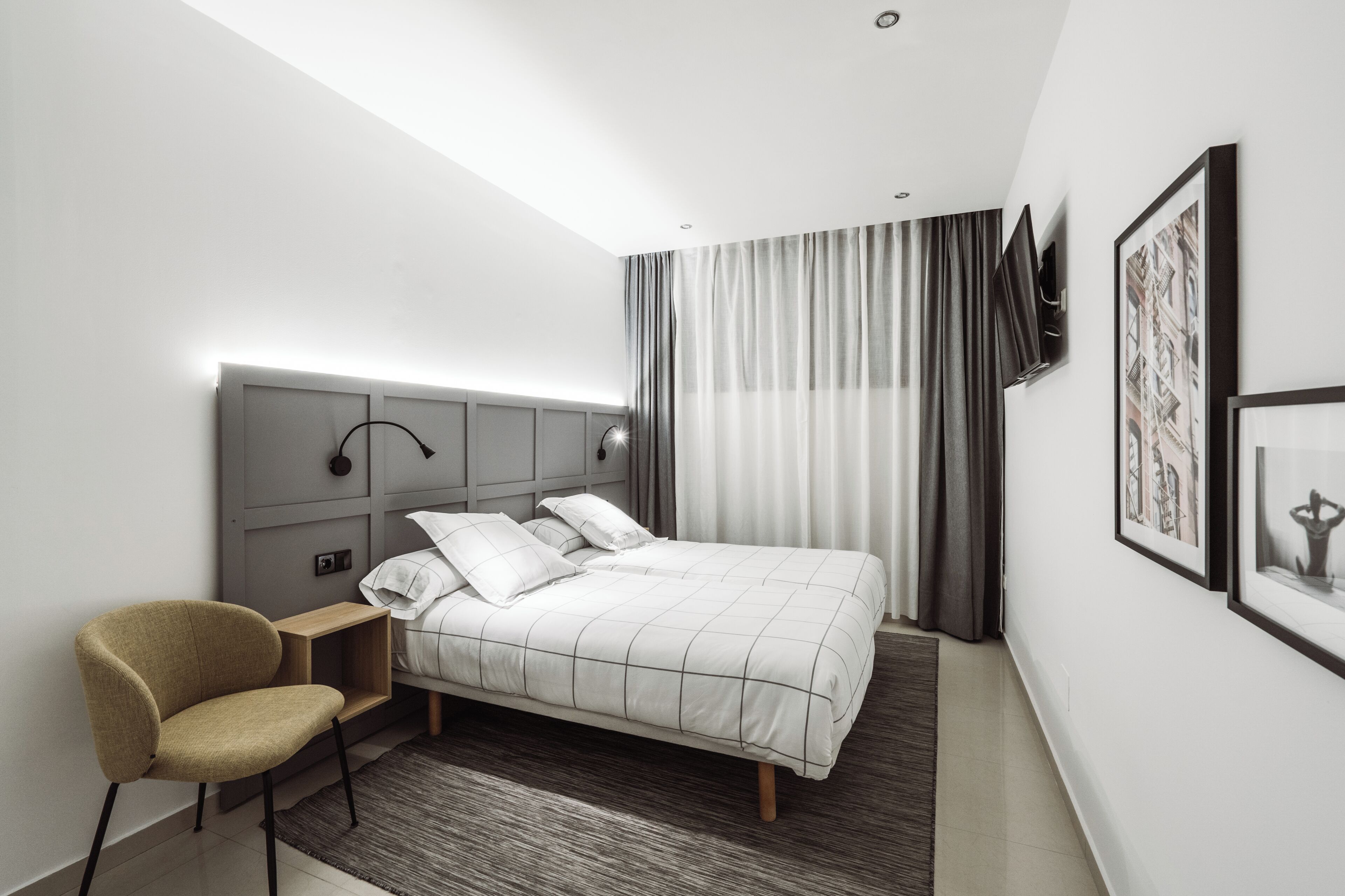 Une chambre d’hôtel moderne équipée d’un lit, d’une chaise, d’un téléviseur à écran plat et ornée d’œuvres d’art sur les murs.
