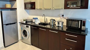 Una cocina moderna con electrodomésticos de acero inoxidable, lavadora integrada y muebles de color marrón oscuro.