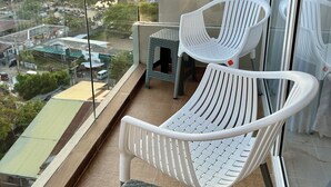 Un balcón con sillas de plástico blanco y una mesa pequeña, con vistas a la costa, edificios y vegetación.