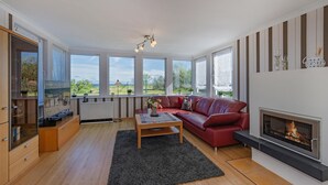Ein modernes Wohnzimmer mit einem roten Sofa, einem Kamin und großen Fenstern mit Blick ins Freie.