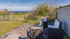 Eine Terrasse im Freien mit Korbmöbeln, einem Glastisch und Blick auf das Meer.