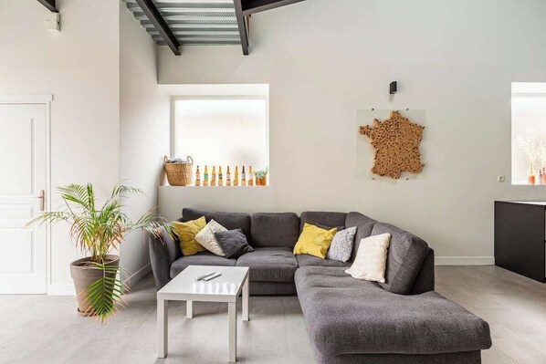 A modern living room with a grey sectional sofa, a white coffee table, and a potted plant.