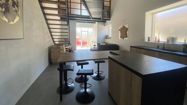 Una cocina moderna con una isla central, taburetes de bar y una escalera que sube a un nivel superior.